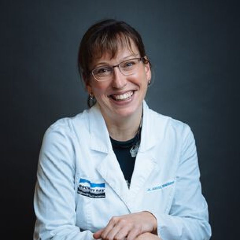 Dr. Astrid Nielssen, DVM, MVSc, DACVIM, Board-certified Internist (Locum), smiling in a white veterinary lab coat with dark background.