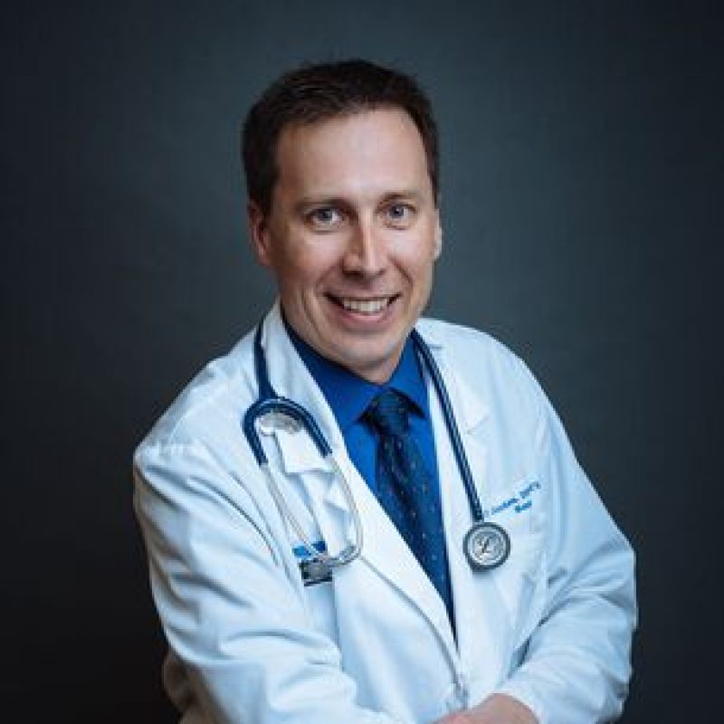 Dr. Peter Gordon, DVM, DACVIM (Neurology), Board-certified Neurologist, wearing a white lab coat with a stethoscope around his neck, smiling against a dark background.