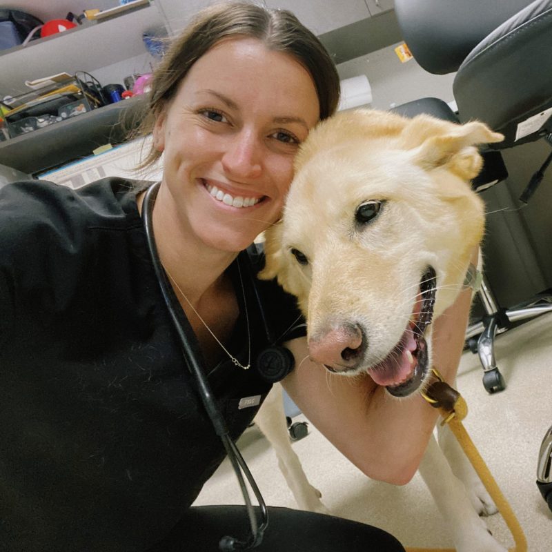 Dr. Elizabeth Meiman, DVM, DACVIM (Neurology), Neurologist, smiling while hugging a golden-colored dog in a veterinary clinic setting.
