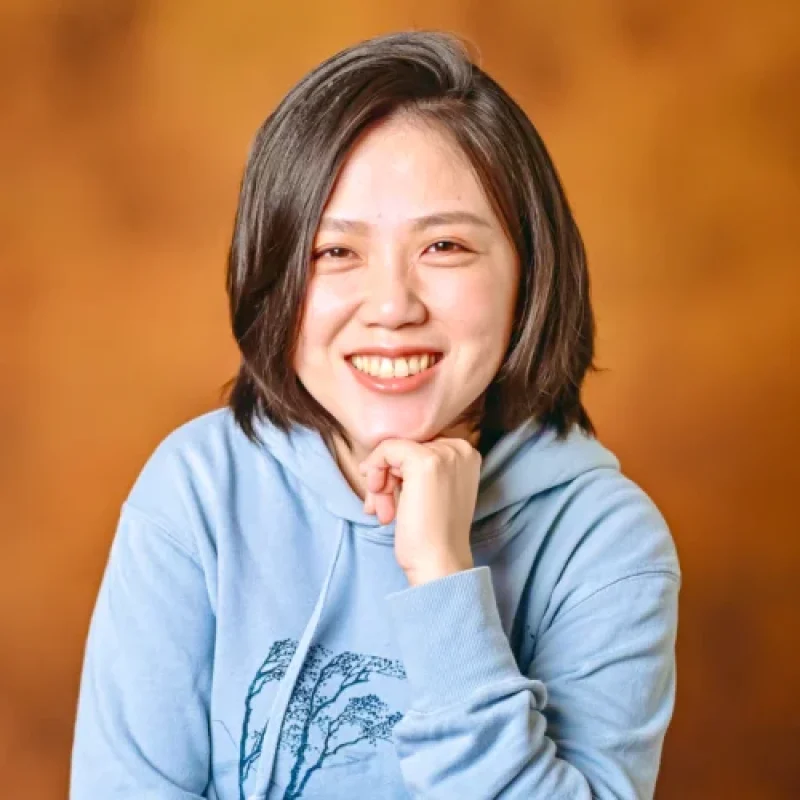 Dr. Lydia (Po-ching) Pan, BVM, MVS, MVSc, DACVIM, Board-certified Internist, smiling in a light blue hoodie with a tree design, posed against a warm orange background.